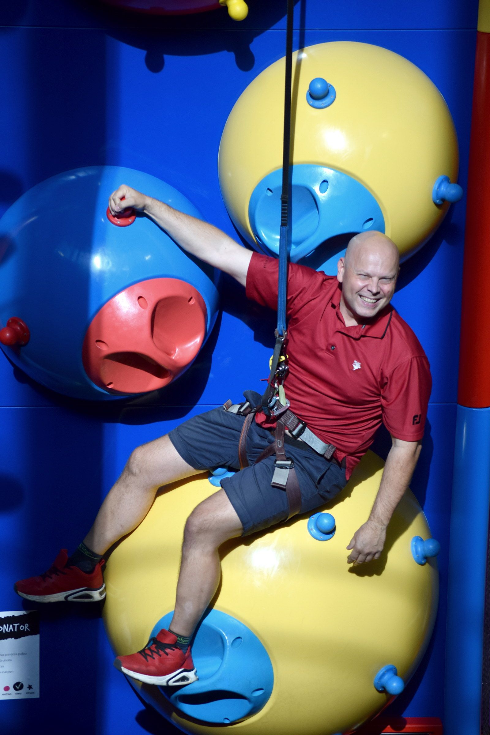 A laughing climber lowered by the auto-belay from yellow and blue ball obstacles