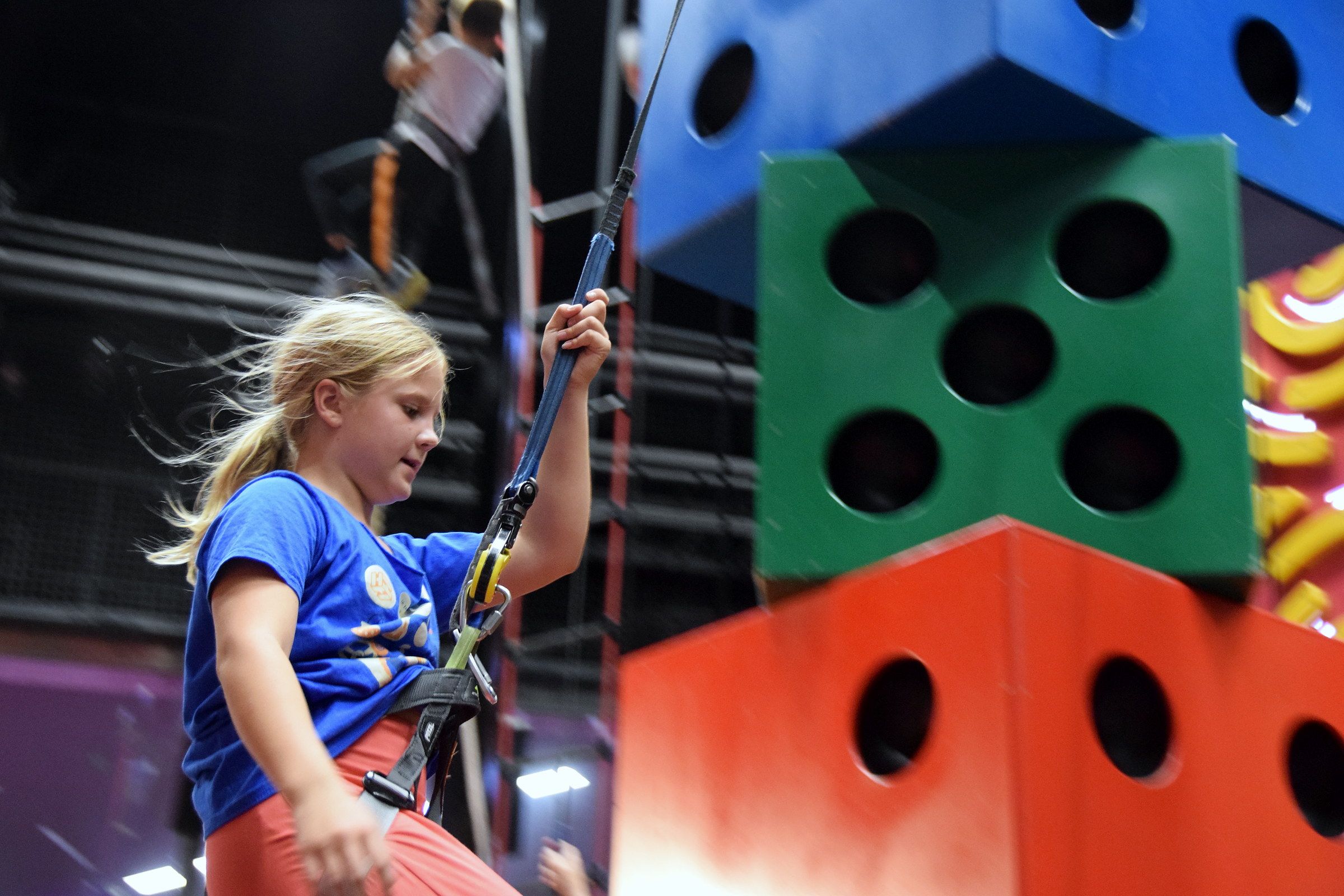 A girl climbing in a harness next to colourful blocks