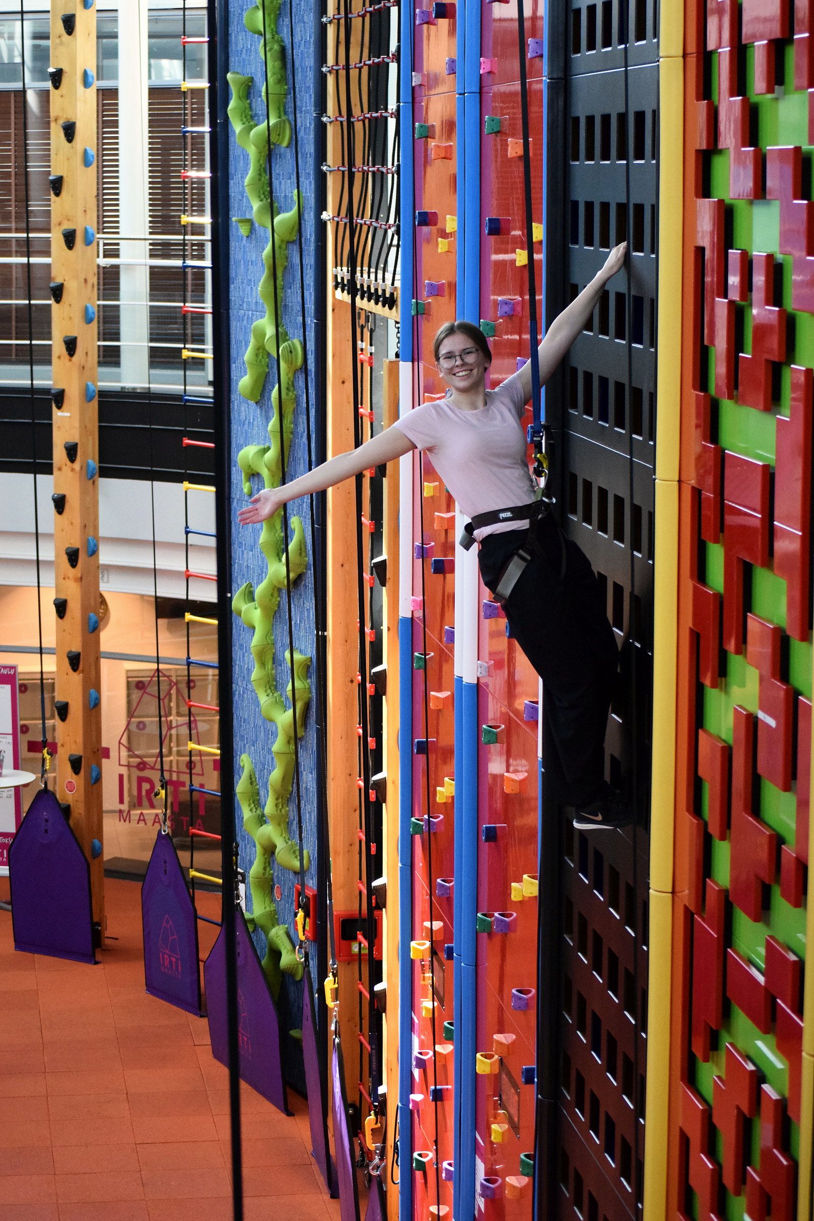 A climber leans back high on the wall, arms wide, held by the auto-belay